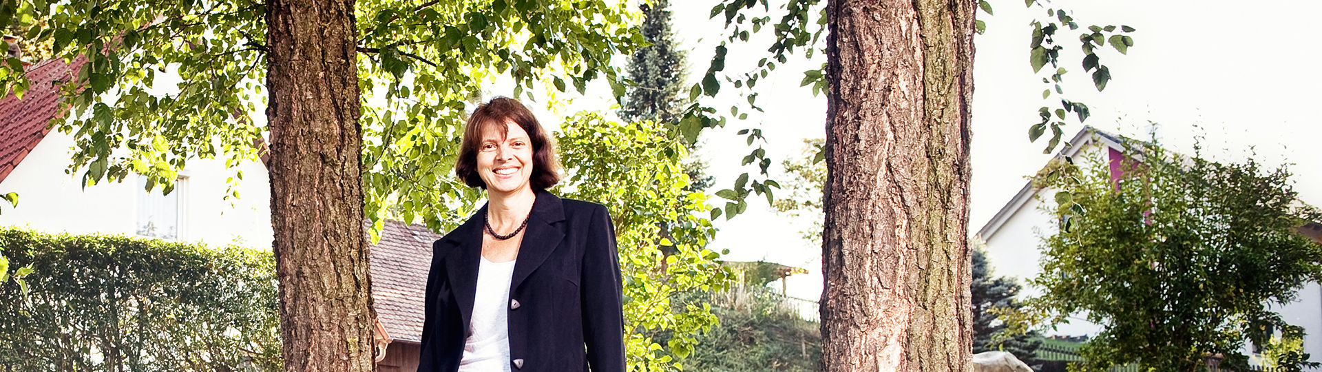 Die Grundschulleiterin steht unter 2 Bäumen und vor der Hecke der Grunschule Berkheim