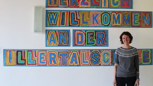 Die Schulleiterin steht vor dem Schriftzug 