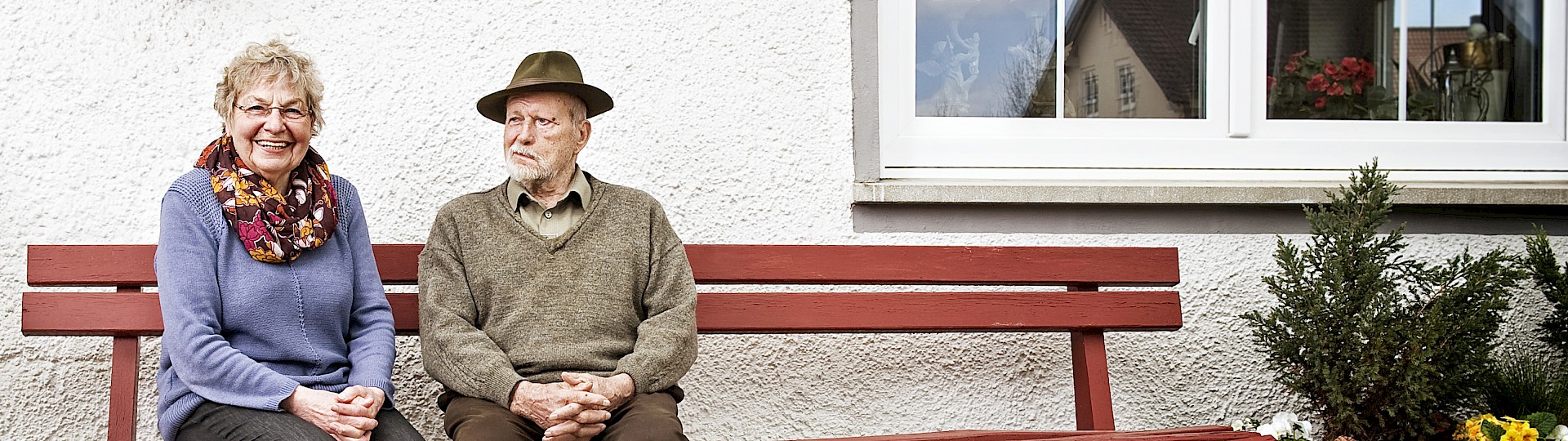 alte Frau und Mann auf einer Gartenbank vor einem Haus